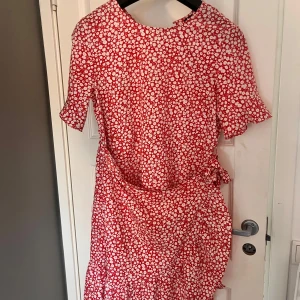 Rödvit blommig klänning från Vero Moda - Säljer en söt röd klänning med vitt blommönster från Vero Moda. Klänningen har korta ärmar med lätt volang och markerad midja. Perfekt för sommarens alla tillfällen. Lätt och luftig modell.