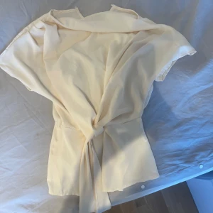 Vit omlottblus med knyt - Säljer en stilren beige omlottblus med knyt i midjan. Blusen har korta ärmar och en lös passform som ger en avslappnad men ändå elegant look. Perfekt att styla till olika tillfällen!