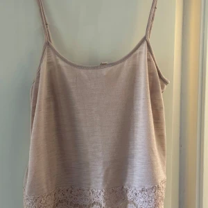 Beige linnetopp med spetskant - Säljer en rosa  linnetopp med tunna axelband och dekorativ spetskant längst ner. Toppen har en enkel och stilren design, perfekt för varma dagar. Detta linne är köpt på HM i storlek M. Priset kan diskuteras!
