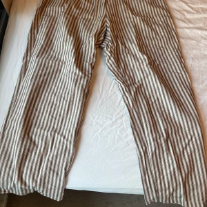 Randiga byxor med snörning - Snygga linne byxor med beige och vita ränder och avslappnad passform. Byxorna har resår i midjan och snörning framtill för extra komfort. Perfekta för en chill och stilren look. Storlek XXL som sitter som en L, köpt på Nelly för något år sedan
