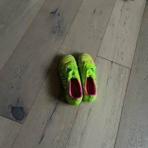 Adidas Predator fotbollsskor i neonfärg - Säljer ett par Adidas Predator nästan helt nya fotbollsskor i neon-gul med rosa och blå detaljer. Skorna har snörning och är designade för att ge bra grepp på planen med sina dobbar. Perfekta för dig som vill sticka ut på fotbollsplanen!
