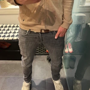 Grå jeans från Jack & Jones - Säljer ett par grå jeans från Jack & Jones i storlek 30/32. Passformen är slim/glenn och jeansen sitter riktigt bra längst bena. Liten defekt på baklappen som syns på sista bilden, annars helt defektfria. Jag är runt 190 så de sitter lite större än storleken. Vid minsta fråga är de bara att höra av sig! Pris kan diskuteras om snabb affär.
