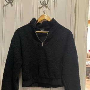 Svart fleece-tröja med dragkedja från Gina Tricot - Mysig svart fleece-tröja från Gina Tricot med halv dragkedja framtill och hög krage. Tröjan har lång ärm och är croppad i modellen, perfekt för kyliga dagar. Superfint skick