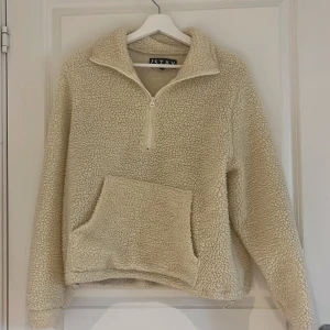 Beige fleece-tröja från Stay - Mysig beige fleece-tröja från Stay med halv dragkedja och stor magficka. Tröjan har hög krage och långa ärmar, perfekt för kyliga dagar. Supermjuk och fluffig känsla.