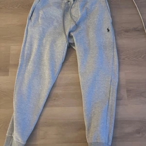 Grå mjukisbyxor från Polo Ralph Lauren - Säljer ett par grå mjukisbyxor från Polo Ralph Lauren med dragsko i midjan och fickor på sidorna. Byxorna har en liten broderad logga på vänster sida och muddar vid bensluten. Perfekta för en avslappnad stil.