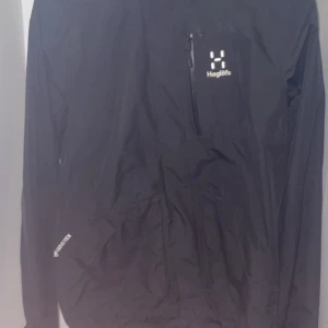  Haglöfs jacka GORTEX  - Säljer en svart vindjacka från Haglöfs med huva och dragkedja på bröstet. Jackan har lång ärm och är perfekt för utomhusaktiviteter. Klassisk och stilren design med Haglöfs-logga på bröstet.