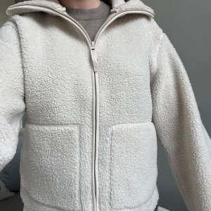 Vit teddyjacka med dragkedja från H&M - Populär vit teddyjacka med dragkedja framtill och två stora fickor. Jackan har hög krage och lång ärm, perfekt för kallare sommarkvällar!🩷använd 2ggr 