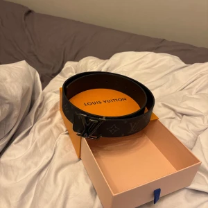 Svart bälte från Louis Vuitton - Säljer ett svart bälte från Louis Vuitton med klassiskt monogrammönster och svart spänne. Bältet är gjort i skinn och levereras i originalförpackning. Perfekt accessoar för att lyfta din outfit. Jag har även digitalt och fysiskt kvitto.