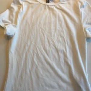 Vit t-shirt från Bershka - En klassisk vit t-shirt från Bershka i mjuk bomull. T-shirten har rund halsringning och korta ärmar, perfekt för en enkel och stilren look. Passar till det mesta och är ett måste i garderoben.