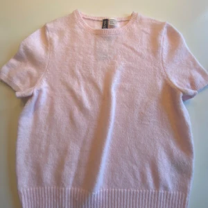 Ljusrosa stickad kortärmad tröja från Divided - Söt ljusrosa stickad tröja från Divided med korta ärmar och rund halsringning. Tröjan har ribbade muddar nedtill och vid ärmsluten, perfekt för en mjuk och avslappnad stil.