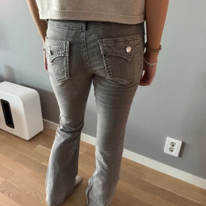 Grå jeansbyxor med fickdetaljer - Snygga lågmidjade grå jeansbyxor med raka ben och dekorativa fickor bak med knappdetaljer. Klassisk femficksmodell och normal passform. Perfekta till vardags för en avslappnad men stilren look.