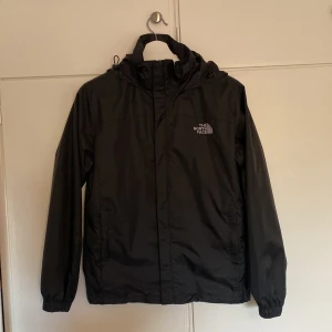 Svart vindjacka från The North Face - Säljer en svart vindjacka från The North Face med huva och dragkedja. Det står storlek M men passar mer som en S-XS. Den har blivit väldigt snålsamt använd och är helt fläckfri och hålfri