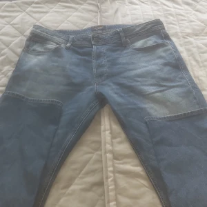 Blå jeansbyxor med klassisk passform - Säljer ett par blå jeansbyxor med klassisk femficksdesign och ljusa slitningar framtill. Byxorna har normal passform och raka ben. Midjemått är W36 och längd L32. Perfekta för en avslappnad stil.