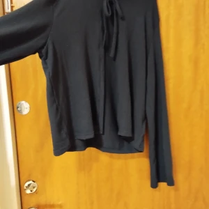 Svart långärmad topp med knyt - Svart långärmad topp med knyt framtill. Enkel och stilren design som passar till många olika outfits. Mjuk och skön att ha på sig, perfekt för både vardag och när du vill klä upp dig lite extra.