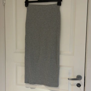 Grå långkjol i bomull - En enkel och stilren grå långkjol i mjukt bomullsmaterial. Kjolen har rak passform och är perfekt för en avslappnad look. Passar till både sneakers och sandaler.