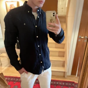 Mörkblå linneskjorta från Morris - Säljer en mörkblå långärmad skjorta från Morris i 100% linne. Skjortan har klassisk krage, knappar framtill och en liten broderad logga på bröstet. Perfekt för dig som gillar stilrena och tidlösa plagg.