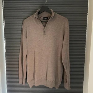 Beige halvzip-tröja från Sand Copenhagen - Säljer en stilren beige stickad tröja från Sand Copenhagen med halv dragkedja och hög krage. Diskret broderad logga på bröstet. Bra skick. Tveka inte att höra av dig vid funderingar!
