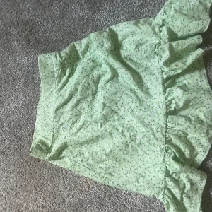 Ljusgrön blommig kjol med volang från Gina Tricot - Supersöt ljusgrön kjol från Gina Tricot med småblommigt mönster och volang nertill. Kjolen är kort och har en bekväm passform, perfekt för varma dagar.