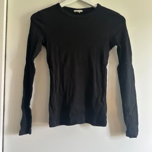 Svart ribbad långärmad topp - En svart, tight och ribbad långärmad topp med rund halsringning. Perfekt basplagg som funkar året runt och är lätt att matcha med olika outfits. Materialet är stretchigt och sitter nära kroppen.