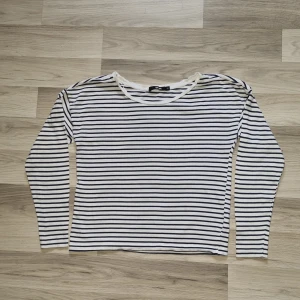 Randig långärmad tröja från Bik Bok - Säljer en klassisk långärmad tröja från Bik Bok i storlek XS. Tröjan är vit med mörkblå horisontella ränder och har en rund halsringning. Perfekt basplagg som är lätt att matcha till olika outfits.