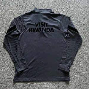 Grå långärmad träningströja från PSG - Säljer en grå långärmad fotbollströja från Paris Saint-Germain med svarta detaljer och röd Nike-logga. Tröjan har dragkedja vid halsen och tryck med 'Accor Live Limitless' samt PSG-emblem på bröstet. Perfekt för träning eller match.