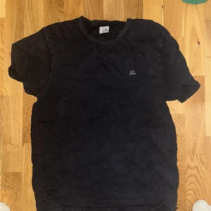 Svart t-shirt från C.P. Company - Säljer en svart t-shirt från C.P. Company med liten logga på bröstet. Klassisk rund halsringning och korta ärmar. Perfekt för en clean och stilren look.