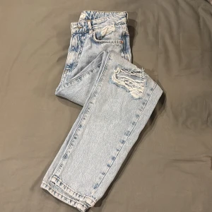 Ljusblå slitna jeans - Säljer ett par ljusblå jeans med slitningar på knäna. Jeansen har raka ben och en avslappnad passform, perfekta för en cool vardagslook.