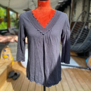 Mörkgrå blus med spets från KappAhl 40/42 - Svart blus med 3/4 ärmar och v-ringning med spetsdetaljer. Blusen har en lätt textur. Längd: 65 cm, bystvidd: 52 cm ﻿92% bomull, 8% elestan  Inga bilder när den sitter på mig! Katter finns i hemmet!