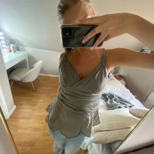 Beige omlott linnetopp med dragkedja - Supersnygg beige omlott linnetopp med smala axelband och v-ringning. Toppen har en lätt volangkant nertill och dragkedja i sidan för enkel påklädning. Nästan aldrig använd och i super fint skick😚💕