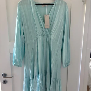 Ljusblå omlottklänning Lemonada - Supersöt ljusblå klänning från Lemonada med omlott-skärning och v-ringad hals. Långa ärmar med resår vid handlederna och volangdetaljer nertill. 