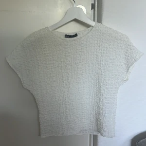 Vit strukturerad topp från Zara - Säljer en vit topp från Zara i storlek S. Toppen har en cool strukturerad yta med korta ärmar och rund halsringning. Den är rak i modellen och känns både modern och enkel att styla till olika looks. Endast testad men var för kort för mig.