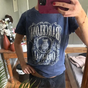 Blå Barcelona t-shirt med tryck - Snygg blå t-shirt med stort vintageinspirerat Barcelona-tryck framtill och motiv av en tjur. Klassisk passform med rund hals och korta ärmar. Perfekt för dig som gillar streetstyle och grafiska prints.