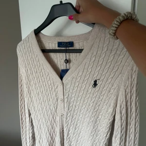 Beige kofta Polo Ralph Lauren - Superfin beige stickad kofta från Polo Ralph Lauren med v-ringning och knappar framtill. Liten broderad logga på bröstet. Helt ny med prislapp kvar, storleken är L men passar mig som S då den är väldigt liten i storlek!