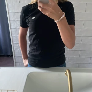 Svart Champion t-shirt i bomull - Svart t-shirt från Champion i storlek L. Klassisk modell med korta ärmar och rund hals. T-shirten har Champion-logga på bröstet och ärmen. Tillverkad i mjuk bomull, perfekt till jeans eller shorts.