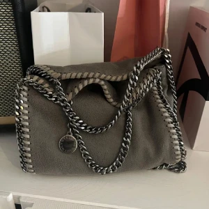 Grå axelväska Stella McCartney - Snygg Stella McCartney väska i fallabella modellen. Det är den minsta. Väskan är använd men i mycket gott skick, enda defekten är en liten prick på brickan med märket (bild 4), men den syns inte om man inte kollar nära. Kan mötas i centrala Stockholm om det önskas. 