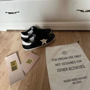 Svarta Golden Goose sneakers - Helt nya Golden Goose sneakers i svart skinn med vit stjärndetalj på sidan och vit häl. Klassisk låg modell med svarta skosnören och platt sula. Märkets logga syns på häl och plös. Snygg streetstil med slitna detaljer och autentisk känsla.