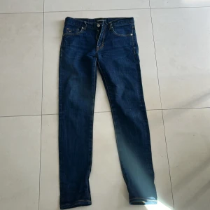 Mörkblå skinny jeans från J.Lindeberg - Snygga mörkblå jeans från J.Lindeberg med klassisk femficksdesign och silverfärgad logga på myntfickan. Jeansen har skinny passform, kontrastsömmar och är tillverkade i stretchig denim för en bekväm känsla. Perfekta till sneakers eller boots.