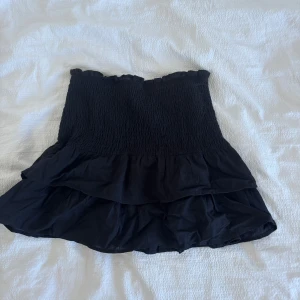 Svart volangkjol med smock - Supersöt svart kortkjol med smockad midja och dubbla volanger. Har en vit likadan och en blå liknanden som går att köpa tillsammans!