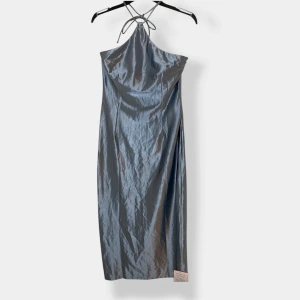 Silvrig blå långklänning från Glamorous - Supersnygg långklänning i skimrande silver blå från Glamorous. Klänningen har halterneck med tunna knytband och en slät, glansig yta som ger en lyxig känsla. Perfekt för dig som vill sticka ut med en elegant och modern look.