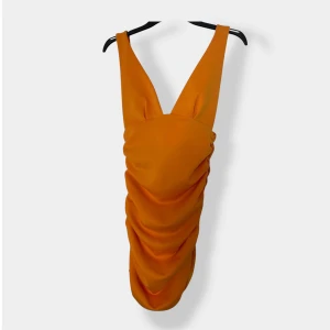 Orange draperad kortklänning ASOS - Snygg orange kortklänning från ASOS med breda axelband och djup v-ringning. Klänningen har en draperad design som ger en cool och trendig look. Perfekt för dig som vill sticka ut med färg och form. Materialet känns mjukt och följsamt.