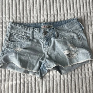 Ljusblå jeansshorts från Guess - Snygga ljusblå jeansshorts från Guess med låg midja. Storlek w25!