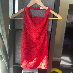 Röd spetsig halterneck topp NA-KD - Säljer en röd halterneck topp från NA-KD i storlek 38. Toppen har vacker spets med blommigt mönster, draperad halsringning och tunna band i ryggen. Perfekt för dig som vill sticka ut med en färgstark och trendig look.