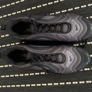 Nike Air Max 720 svarta sneakers - Säljer ett par svarta Nike Air Max 720 sneakers med futuristisk design och vågformade detaljer. Skorna har en hög synlig luftbubbla i sulan, snörning och en rund tå. Perfekta för dig som gillar streetwear och vill ha en riktigt snygg och bekväm sneaker.