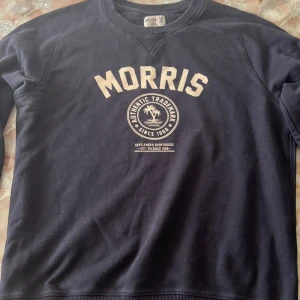 Mörkblå sweatshirt från Morris - Snygg mörkblå sweatshirt från Morris med tryck framtill i beige. Tröjan har rund halsringning, långa ärmar och ribbade muddar. Perfekt för en chill och stilren look. Materialet är mjuk bomull som känns skönt mot huden.