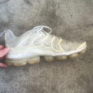 Nike Air Vapormax vita sneakers - Nike Air Vapormax sneakers i vitt med futuristisk design och genomskinlig bubblig sula. Ovandelen har vågformade detaljer och snörning. Perfekta för dig som gillar streetstyle och vill ha en unik look. Snygga till jeans eller shorts.