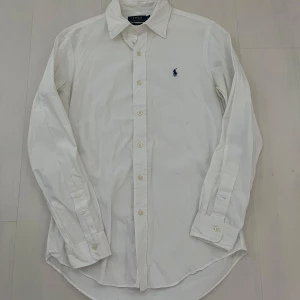 Vit skjorta från Polo Ralph Lauren - Säljer en normal fit vit skjorta från Polo Ralph Lauren med broderad blå logga på bröstet. 9/10 skick. Skicka gärna ett meddelande vid frågor.