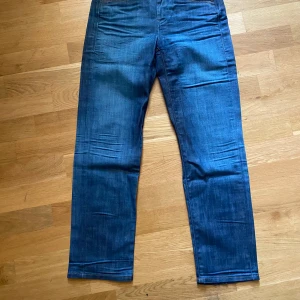 Blå jeans från Wrangler straight fit - Säljer ett par klassiska blå jeans från Wrangler med raka ben och snygga kontrastsömmar. Jeansen har fem fickor, bälteshällor och detaljer med Wrangler-logga på bakfickan. Perfekta för dig som gillar en tidlös och clean look.