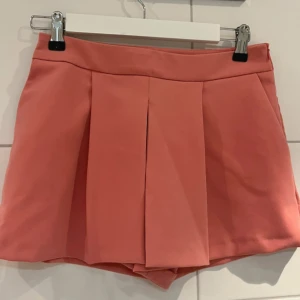 Korallrosa shortskjol från Zara Woman - Superfin korallrosa shorts/kjol från Zara Woman med  veck framtill. Tillverkad i ett mjukt och lätt material. Endast använd en gång 
