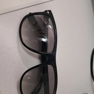 Svarta Ray-Ban Wayfarer solglasögon - Klassiska svarta Ray-Ban Wayfarer RB4147 med bred båge och mörktonade glas. Snygg och tidlös modell med diskret logga på linsen och silvriga detaljer vid bågfästet. Perfekta för att lyfta din stil under soliga dagar.