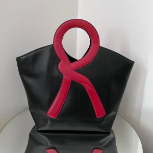 Handväska  - Unik handväska med coolt handtag och dekor i rött. Väskan har en stilren och modern design med rymlig insida. Statement piece för dig som gillar att sticka ut.